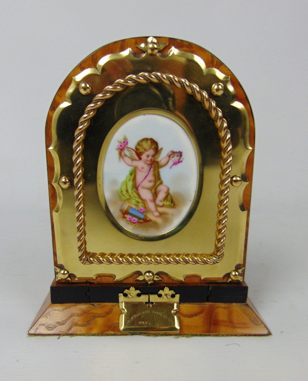An expanding wooden book slide featuring golden burr wood veneer, folding arched ends, and a gilt brass front plate framing an oval painted porcelain cherub medallion. View V