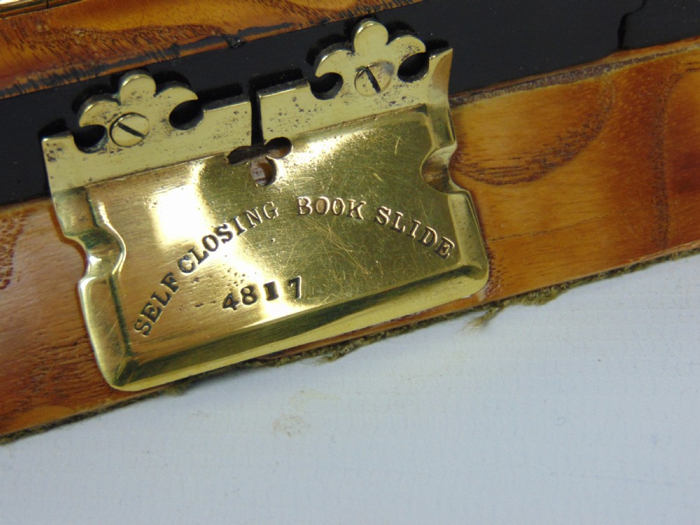 An expanding wooden book slide featuring golden burr wood veneer, folding arched ends, and a gilt brass front plate framing an oval painted porcelain cherub medallion. View VII
