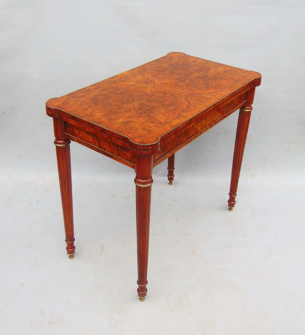 A Victorian burr walnut fold-over card table featuring a figured veneer top, brass beaded edging, and turned fluted legs. View II
