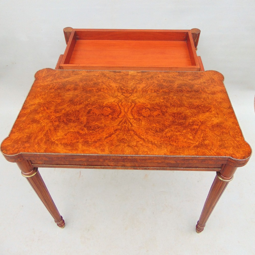 A Victorian burr walnut fold-over card table featuring a figured veneer top, brass beaded edging, and turned fluted legs. View III
