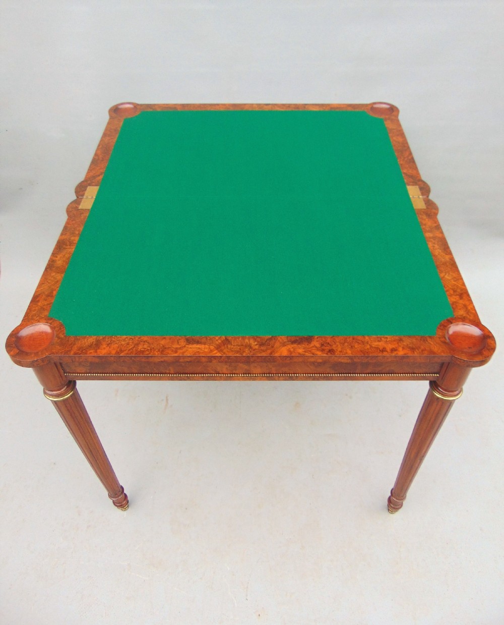 A Victorian burr walnut fold-over card table featuring a figured veneer top, brass beaded edging, and turned fluted legs. View V