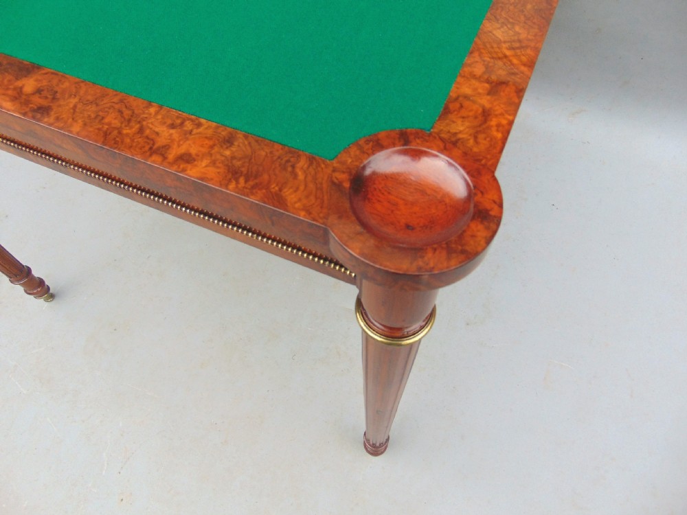 A Victorian burr walnut fold-over card table featuring a figured veneer top, brass beaded edging, and turned fluted legs. View VII
