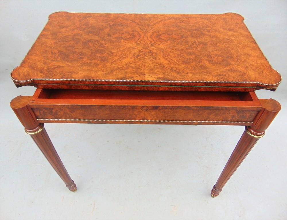 A Victorian burr walnut fold-over card table featuring a figured veneer top, brass beaded edging, and turned fluted legs. View VIII