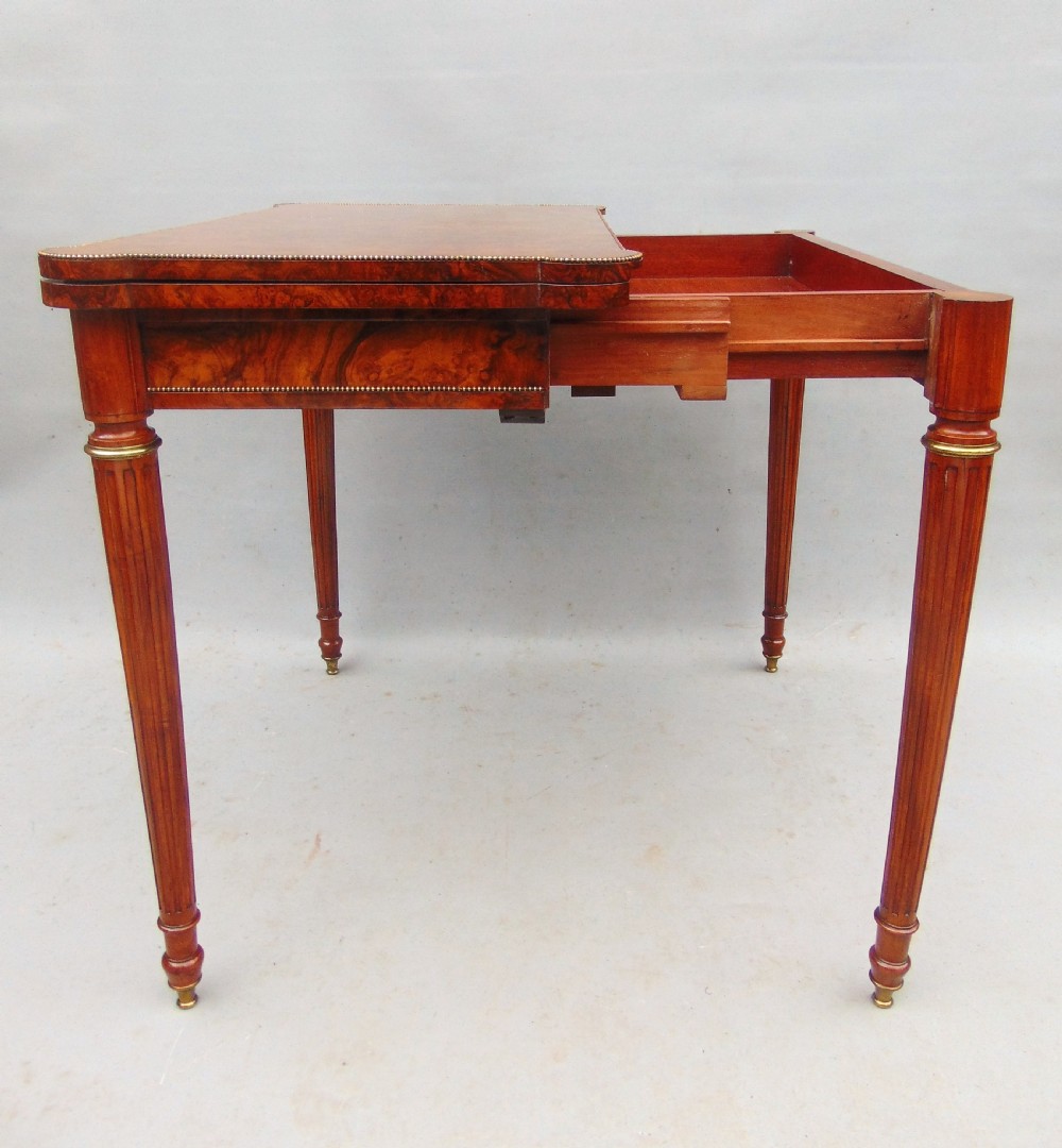 A Victorian burr walnut fold-over card table featuring a figured veneer top, brass beaded edging, and turned fluted legs. View IX