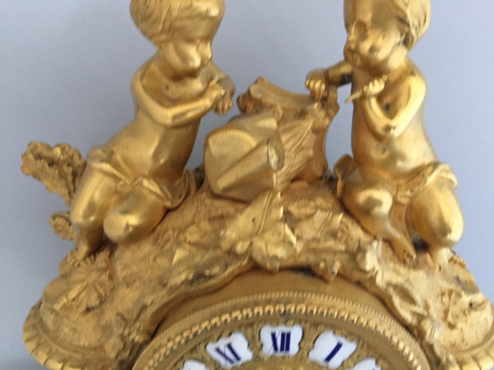 An antique French gilt bronze ormolu mantel clock featuring sculpted cherubs on top and hand-painted blue porcelain panels around a Roman numeral dial. View III