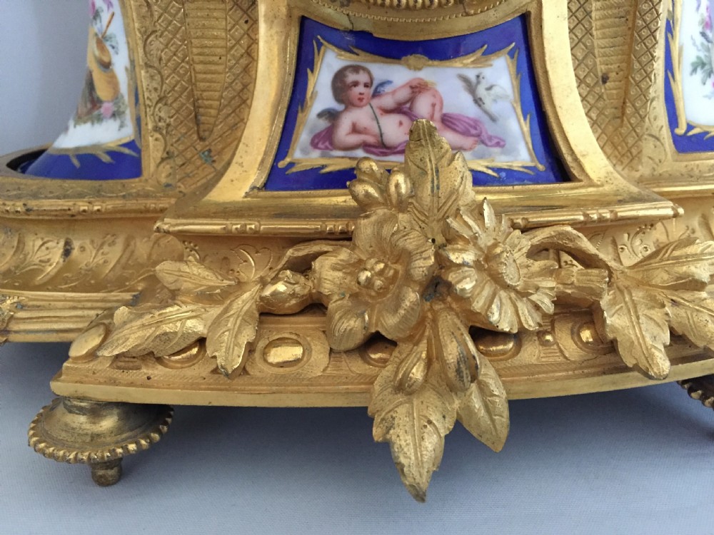 An antique French gilt bronze ormolu mantel clock featuring sculpted cherubs on top and hand-painted blue porcelain panels around a Roman numeral dial. View VI