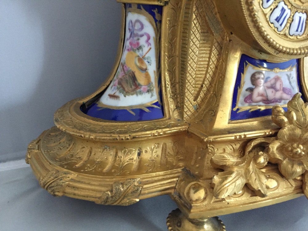 An antique French gilt bronze ormolu mantel clock featuring sculpted cherubs on top and hand-painted blue porcelain panels around a Roman numeral dial. View VII