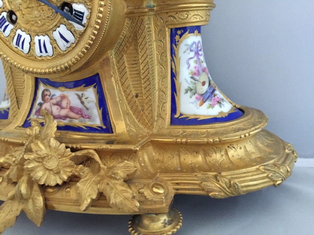 An antique French gilt bronze ormolu mantel clock featuring sculpted cherubs on top and hand-painted blue porcelain panels around a Roman numeral dial. View VIII