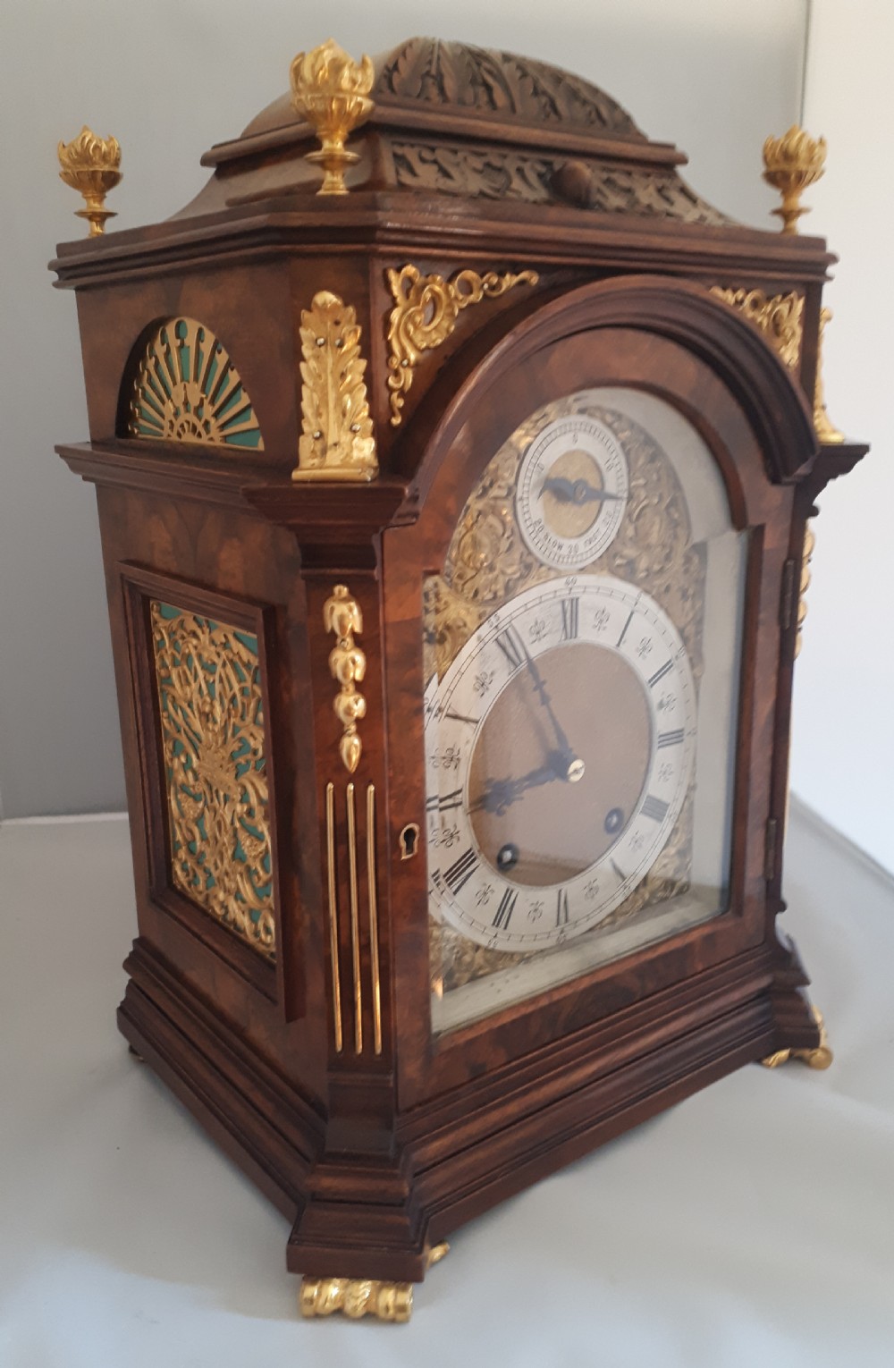 An arched burr walnut bracket clock with ornate gilt brass mounts, finials, and an intricate brass dial displaying Roman numerals. View III