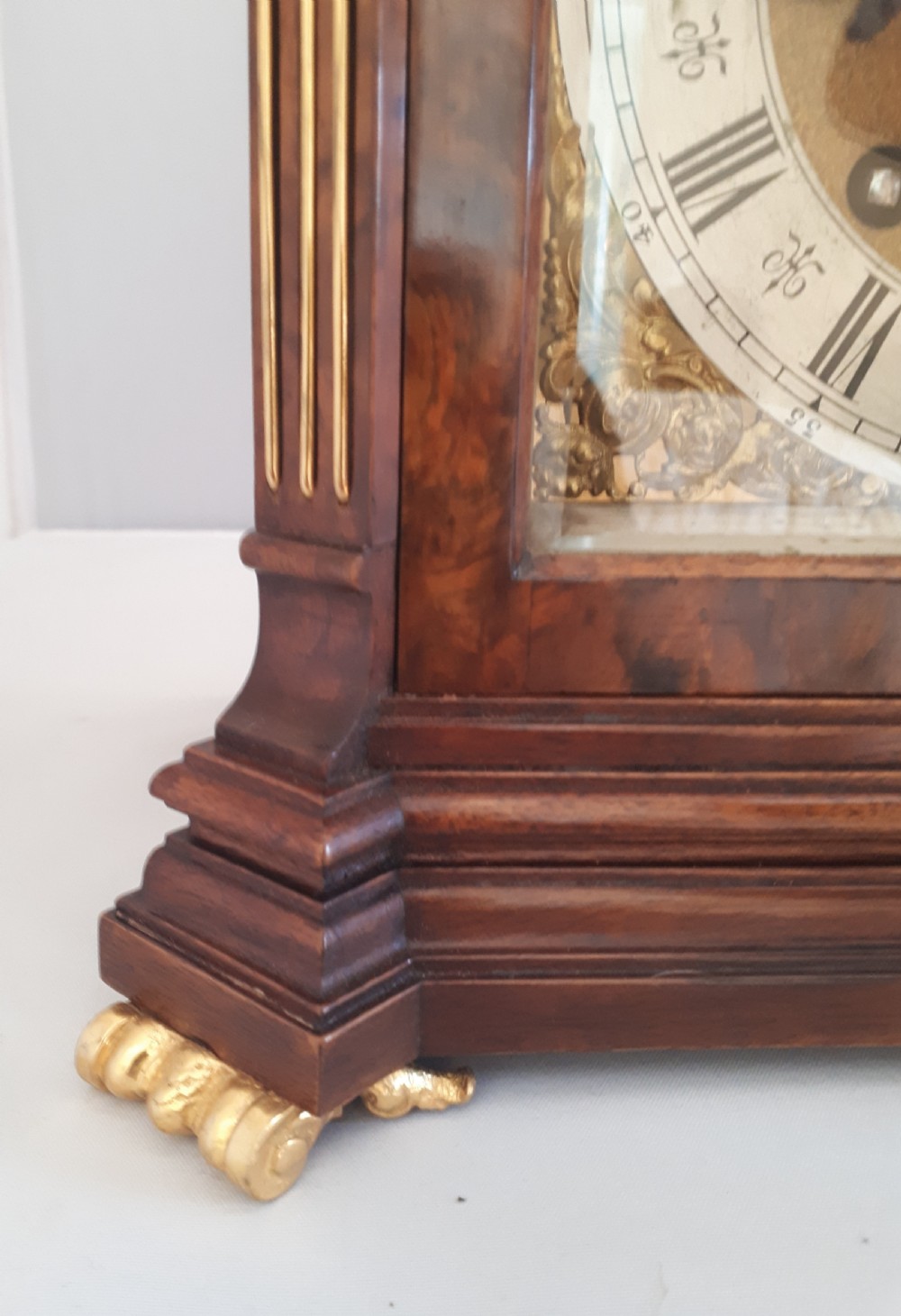 An arched burr walnut bracket clock with ornate gilt brass mounts, finials, and an intricate brass dial displaying Roman numerals. View VIII