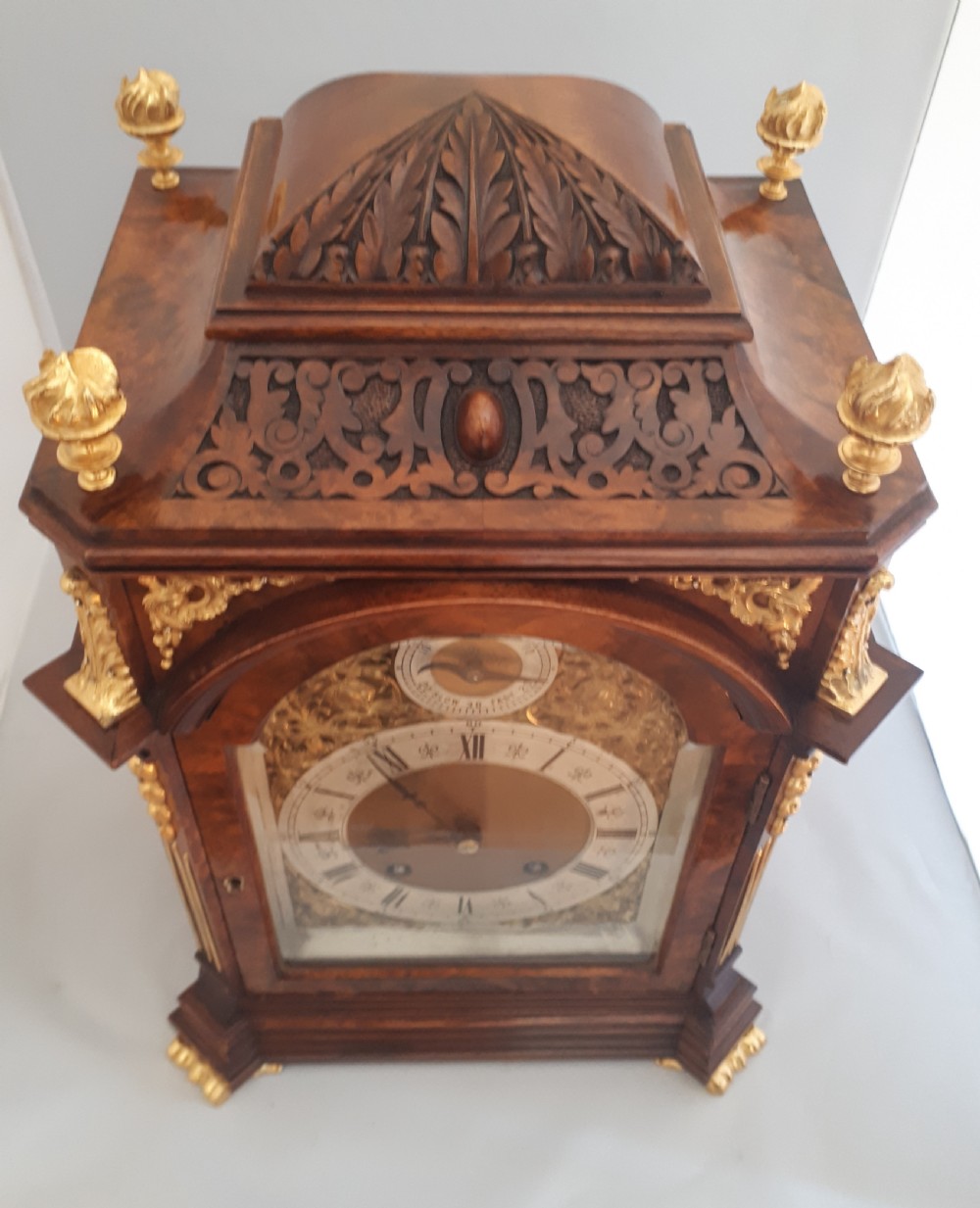 An arched burr walnut bracket clock with ornate gilt brass mounts, finials, and an intricate brass dial displaying Roman numerals. View IX
