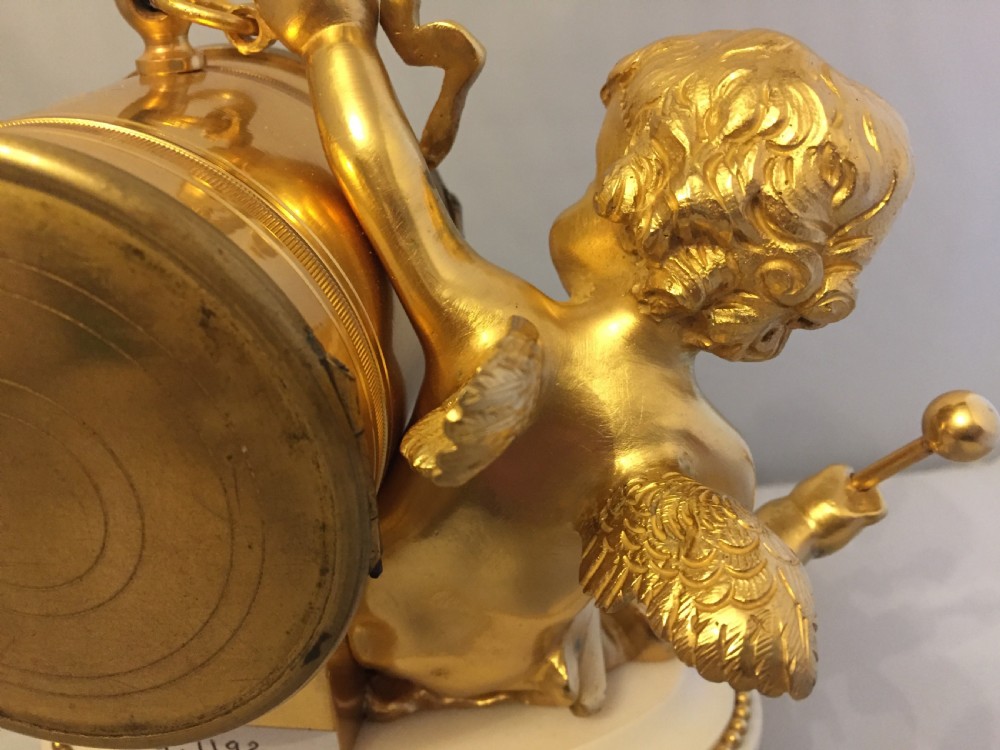 A gilt bronze figure of a cherub reclining on a white marble base while supporting a circular white enamel clock face. View XI