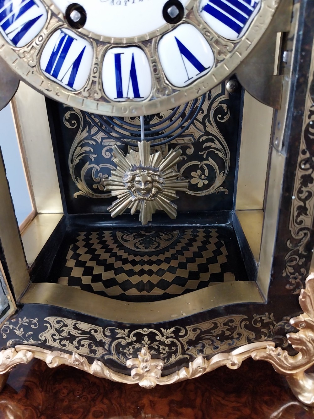 A French Rococo Revival Boulle mantel clock featuring brass marquetry inlay, gilt bronze mounts, an enamel cartouche dial, and a cherub finial. View IV