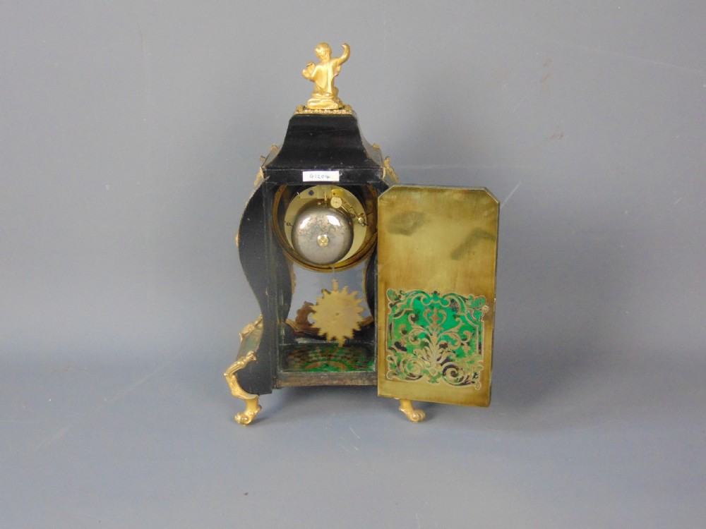 A French Rococo style green Boulle mantel clock featuring brass marquetry inlay, gilded ormolu mounts, a putto finial, and blue enamelled Roman numeral cartouches. View VII