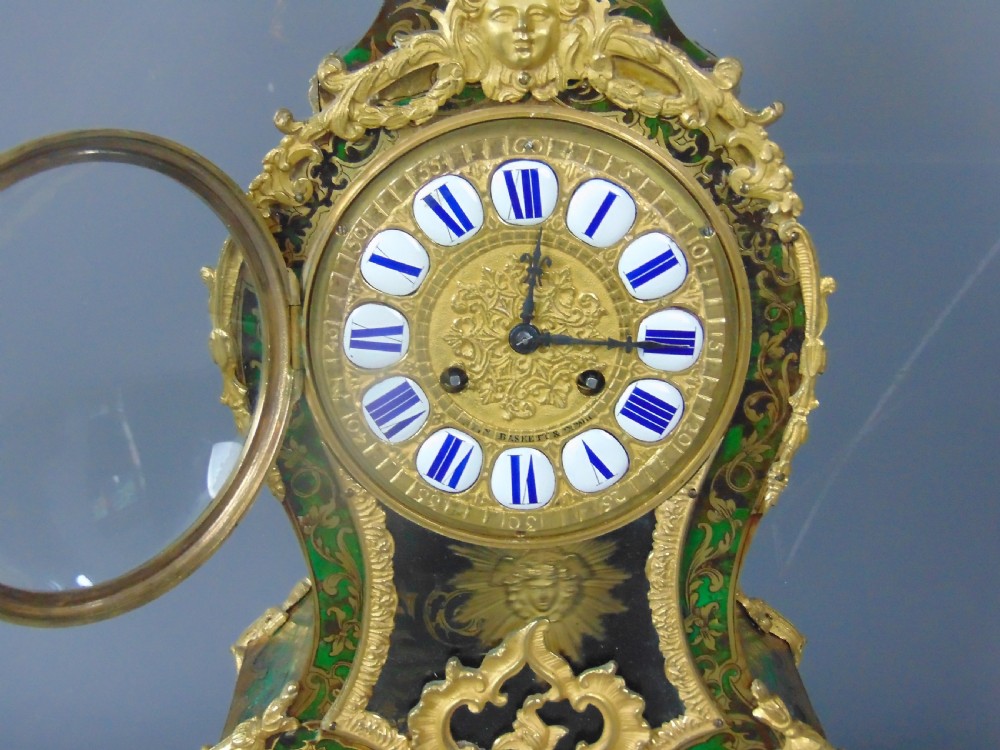 A French Rococo style green Boulle mantel clock featuring brass marquetry inlay, gilded ormolu mounts, a putto finial, and blue enamelled Roman numeral cartouches. View IX