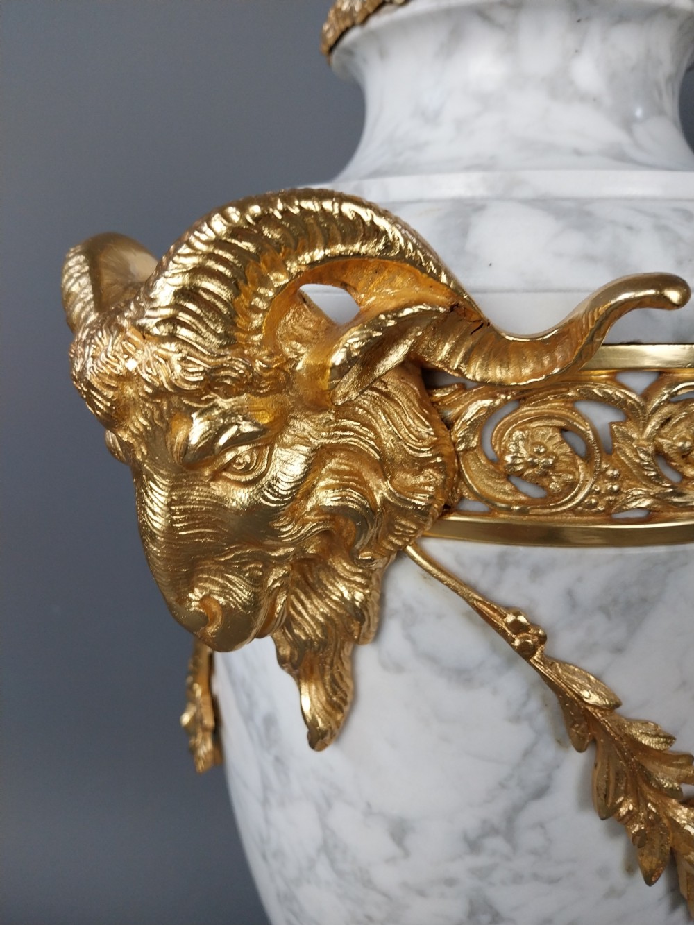 A pair of white veined marble cassolette urns decorated with gilt bronze mounts, floral swags, ram head handles, and finial lids on square bases. View XIII