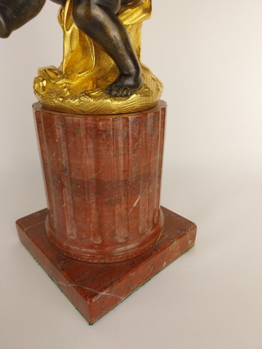 A patinated bronze cherub figure holding two scrolling branches with gilt sconces, set upon a round fluted red marble plinth. View V