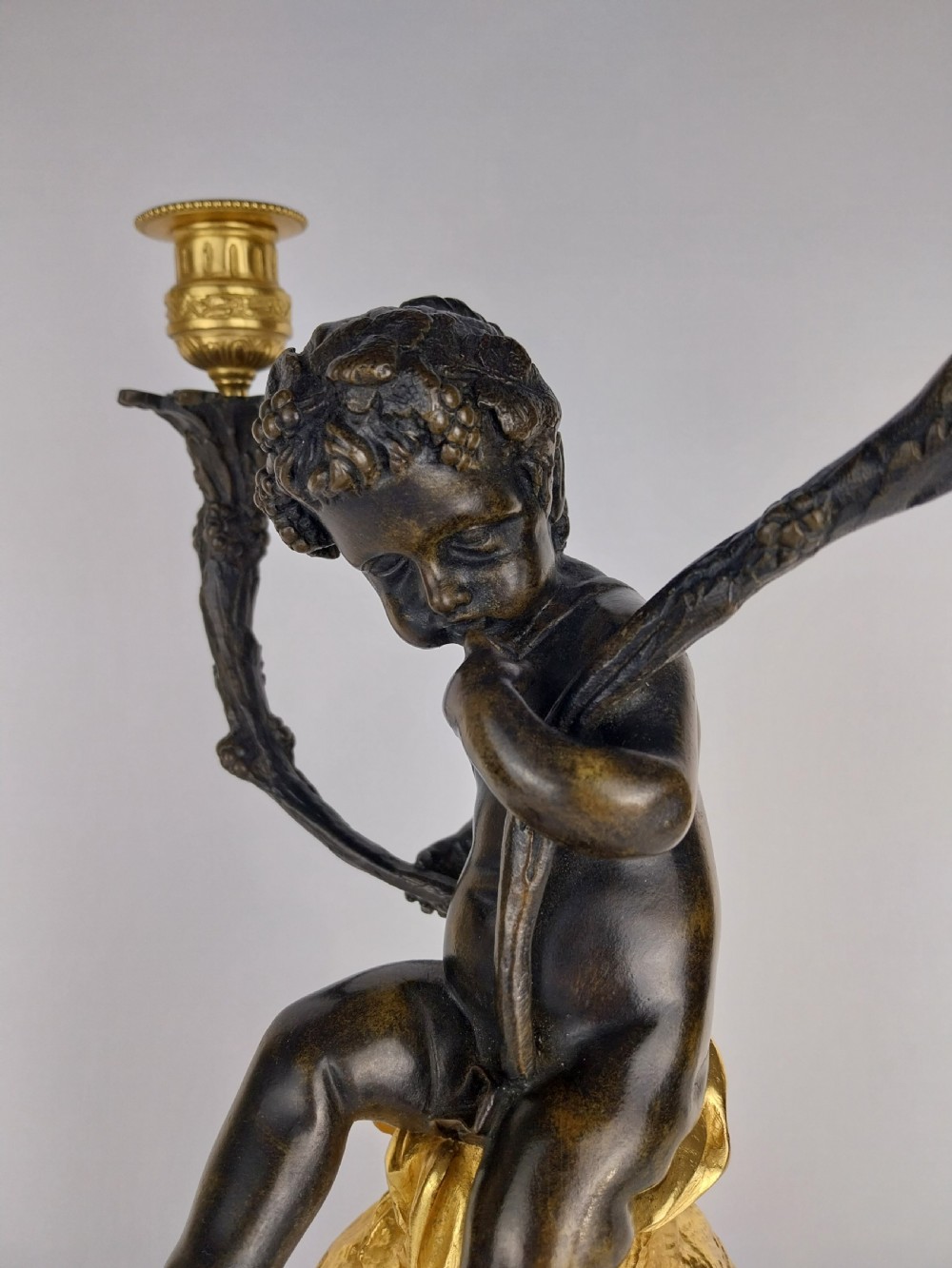 A patinated bronze cherub figure holding two scrolling branches with gilt sconces, set upon a round fluted red marble plinth. View VI