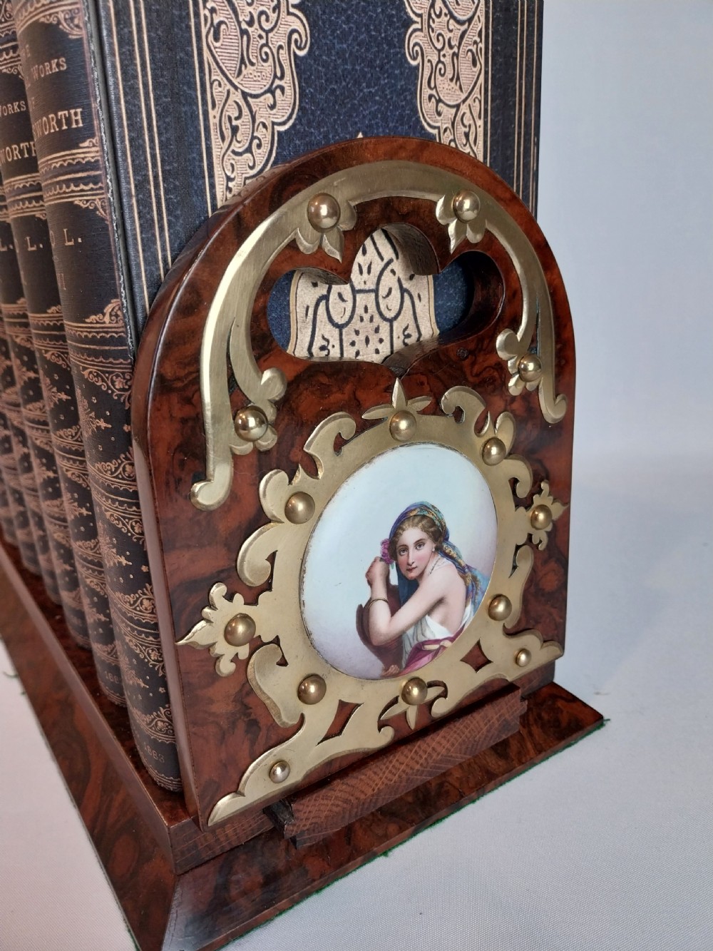 A Victorian burr walnut sliding book slide features pierced brass mounts, decorative studs, and a central painted porcelain plaque. View VI