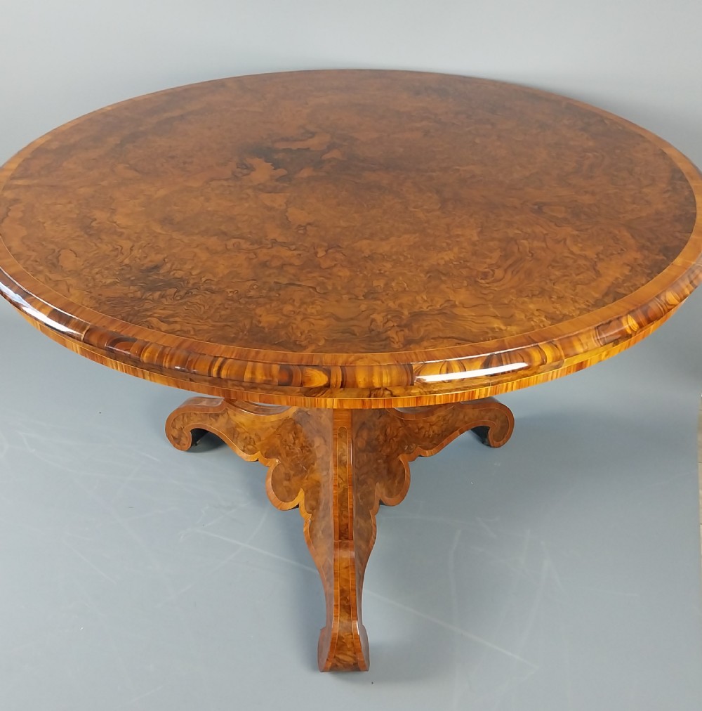 A nineteenth-century circular burr walnut centre table featuring a highly figured top, crossbanded border, and a carved pedestal on four scroll feet. View II