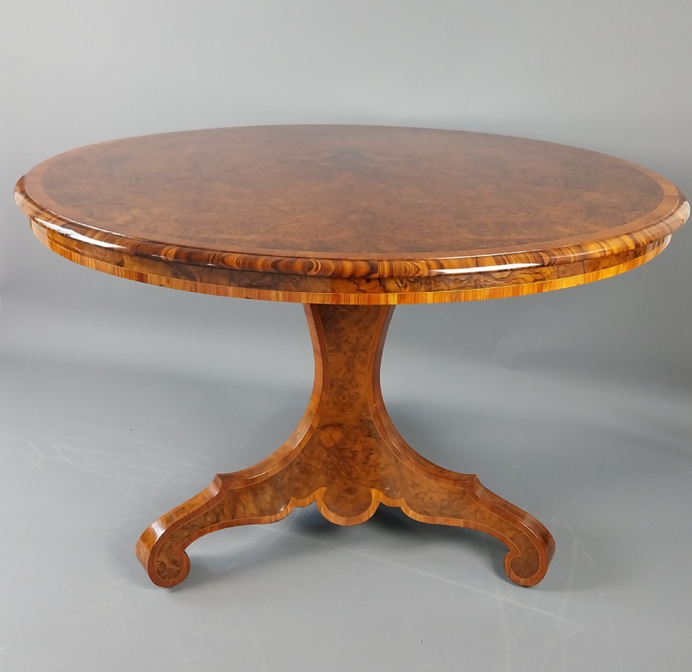 A nineteenth-century circular burr walnut centre table featuring a highly figured top, crossbanded border, and a carved pedestal on four scroll feet. View III