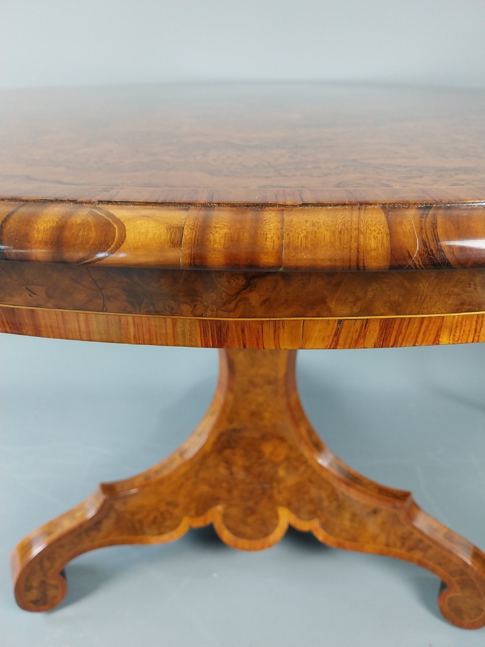 A nineteenth-century circular burr walnut centre table featuring a highly figured top, crossbanded border, and a carved pedestal on four scroll feet. View VI