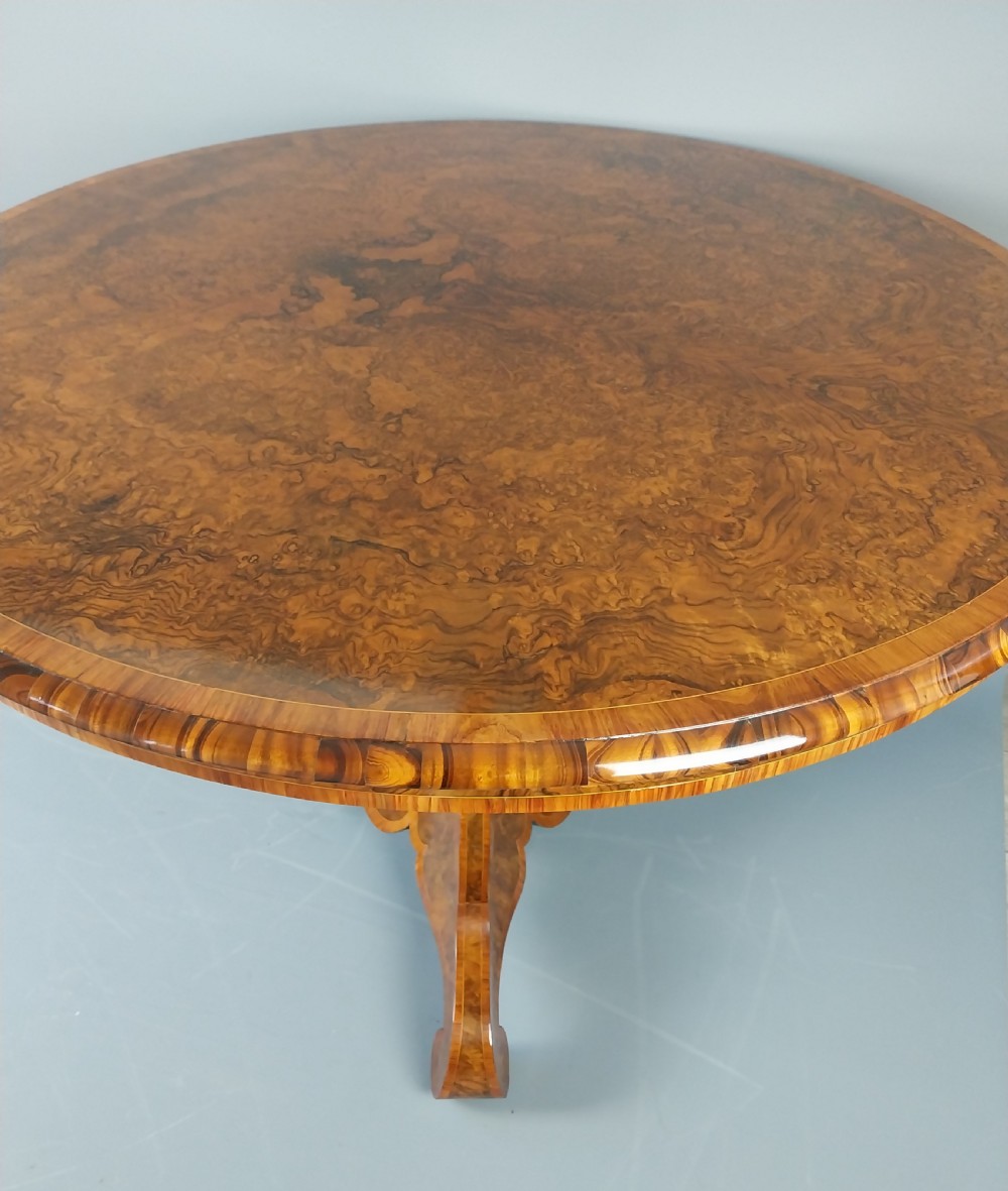 A nineteenth-century circular burr walnut centre table featuring a highly figured top, crossbanded border, and a carved pedestal on four scroll feet. View VII