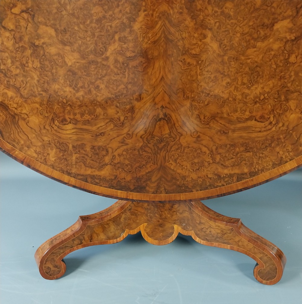 A nineteenth-century circular burr walnut centre table featuring a highly figured top, crossbanded border, and a carved pedestal on four scroll feet. View VIII