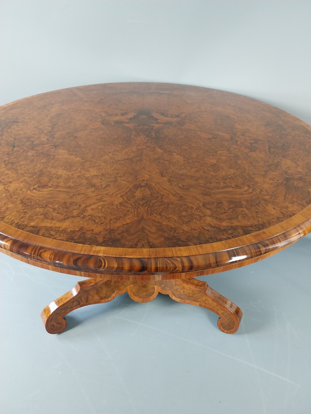 A nineteenth-century circular burr walnut centre table featuring a highly figured top, crossbanded border, and a carved pedestal on four scroll feet. View IX