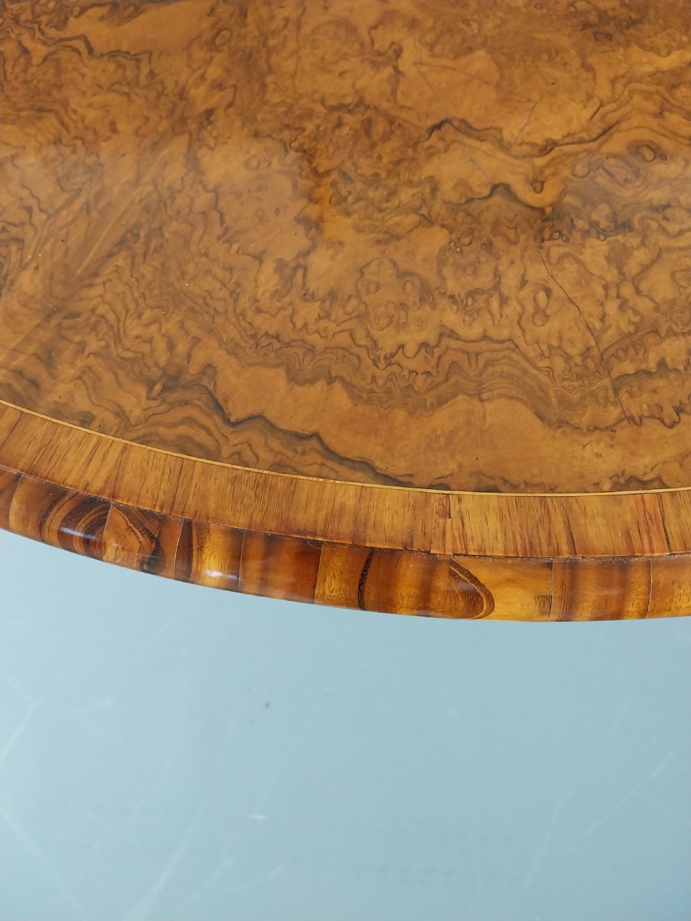 A nineteenth-century circular burr walnut centre table featuring a highly figured top, crossbanded border, and a carved pedestal on four scroll feet. View X