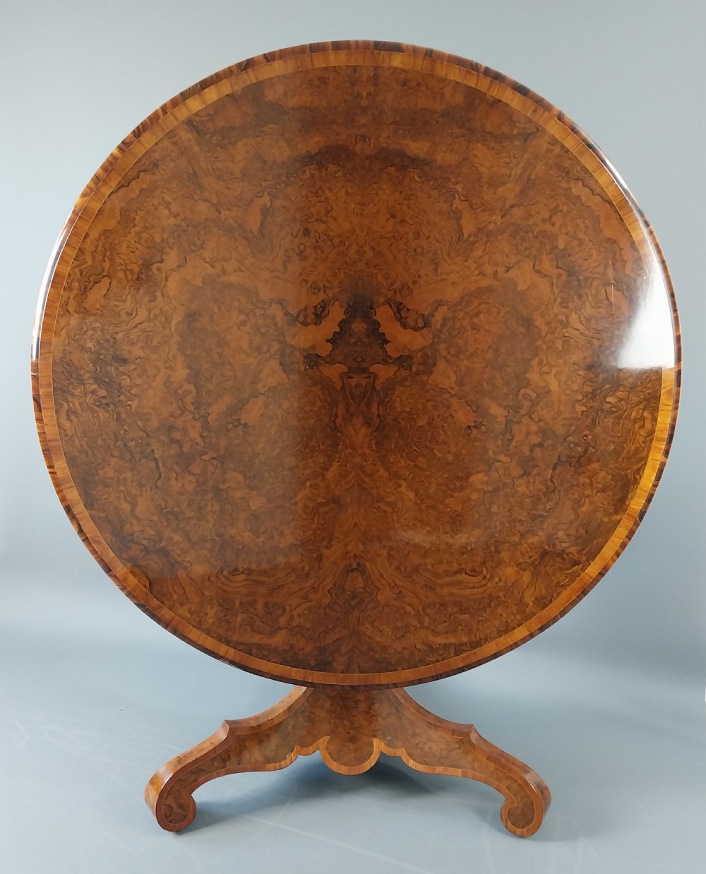 A nineteenth-century circular burr walnut centre table featuring a highly figured top, crossbanded border, and a carved pedestal on four scroll feet. View XI
