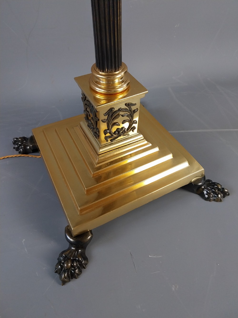 An antique Neoclassical gilt bronze floor standard lamp featuring a fluted dark column, Corinthian capital, stepped square plinth base on claw feet, and a cream fringed shade. View VI