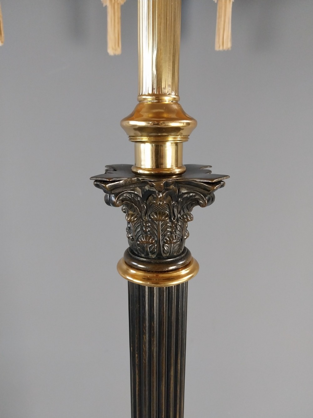 An antique Neoclassical gilt bronze floor standard lamp featuring a fluted dark column, Corinthian capital, stepped square plinth base on claw feet, and a cream fringed shade. View X