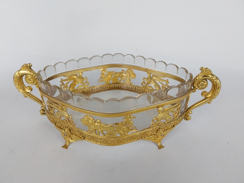 An oval cut glass bowl with a scalloped rim housed within an ornate gilt bronze mount featuring winged sphinxes, lion chariots, and scrolled handles. View II