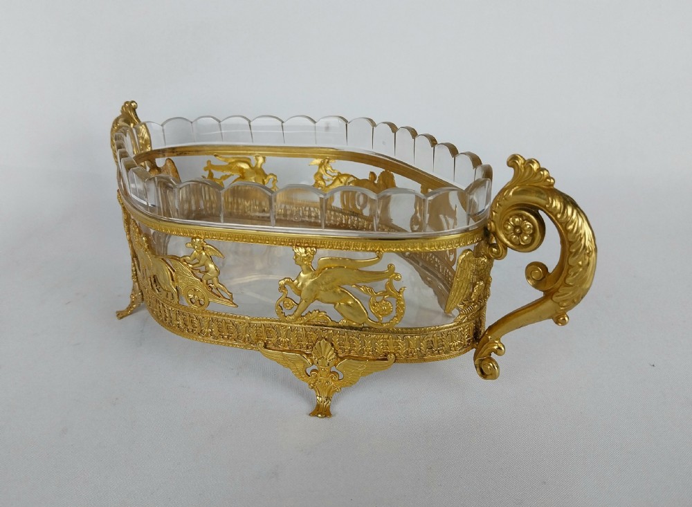 An oval cut glass bowl with a scalloped rim housed within an ornate gilt bronze mount featuring winged sphinxes, lion chariots, and scrolled handles. View III