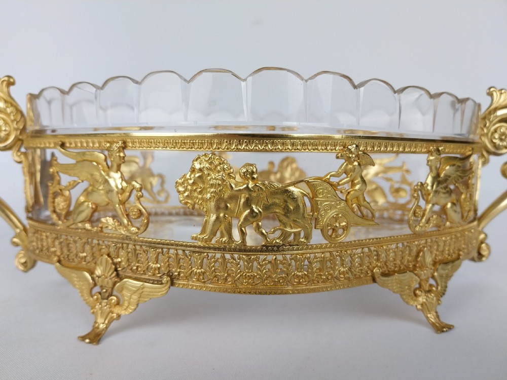 An oval cut glass bowl with a scalloped rim housed within an ornate gilt bronze mount featuring winged sphinxes, lion chariots, and scrolled handles. View V
