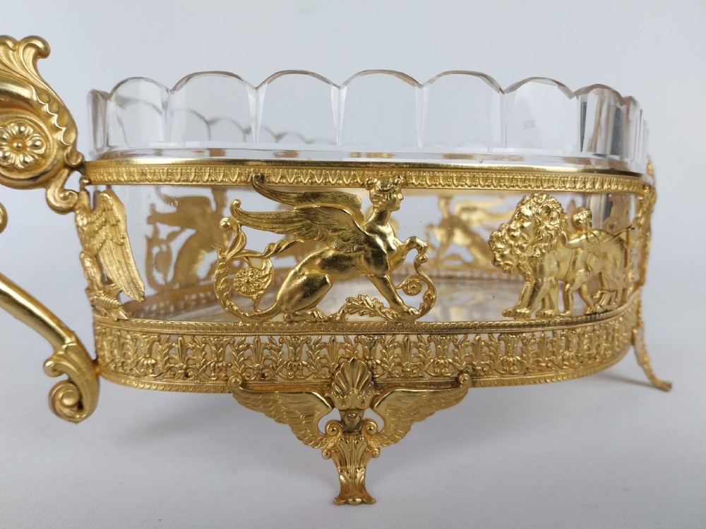 An oval cut glass bowl with a scalloped rim housed within an ornate gilt bronze mount featuring winged sphinxes, lion chariots, and scrolled handles. View VI
