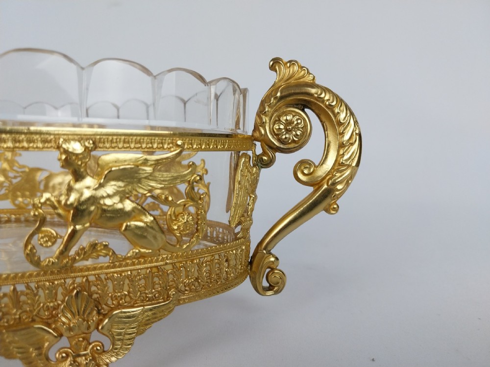 An oval cut glass bowl with a scalloped rim housed within an ornate gilt bronze mount featuring winged sphinxes, lion chariots, and scrolled handles. View VII