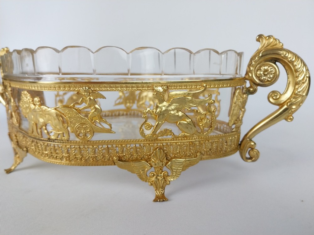 An oval cut glass bowl with a scalloped rim housed within an ornate gilt bronze mount featuring winged sphinxes, lion chariots, and scrolled handles. View VIII