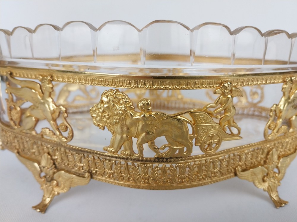 An oval cut glass bowl with a scalloped rim housed within an ornate gilt bronze mount featuring winged sphinxes, lion chariots, and scrolled handles. View IX