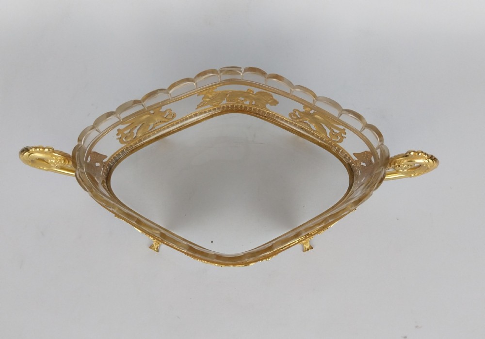 An oval cut glass bowl with a scalloped rim housed within an ornate gilt bronze mount featuring winged sphinxes, lion chariots, and scrolled handles. View XI