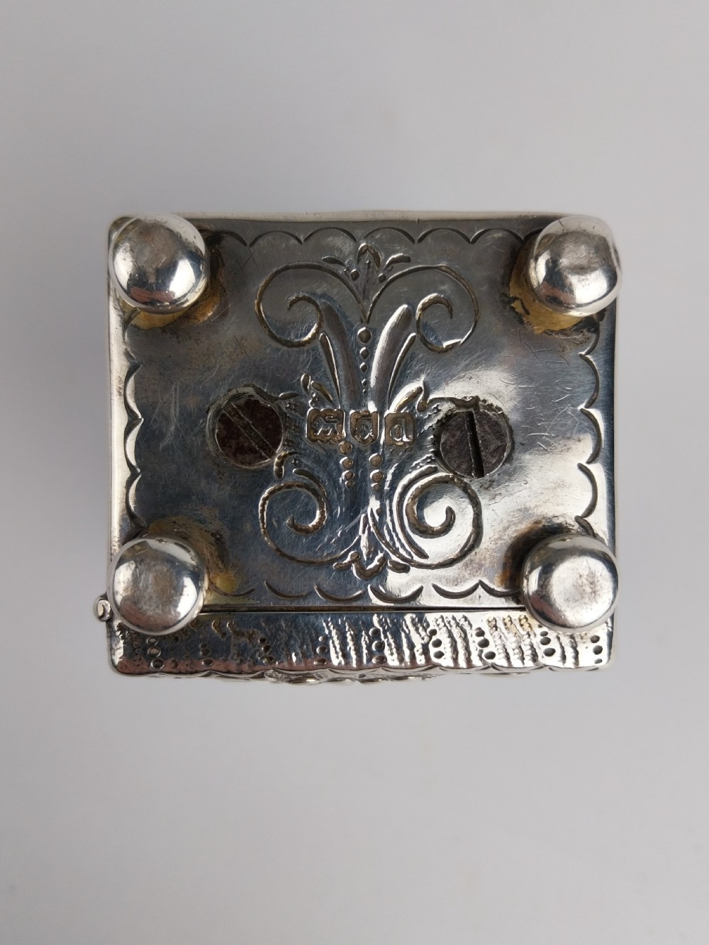A rectangular miniature silver carriage clock featuring floral relief chasing, a curved carrying handle, ball feet, and a white enamel dial with Roman numerals. View X