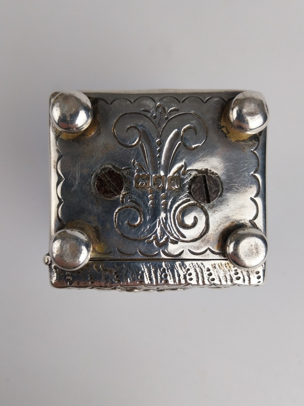 A rectangular miniature silver carriage clock featuring floral relief chasing, a curved carrying handle, ball feet, and a white enamel dial with Roman numerals. View XI