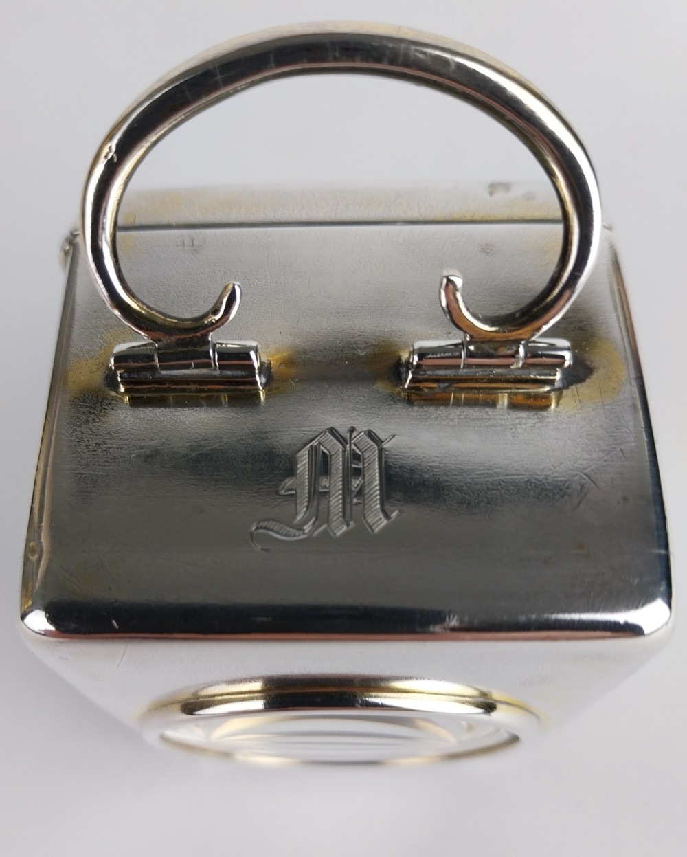 A miniature rectangular silver carriage clock with a curved top loop handle, bun feet, and a white circular dial featuring black Roman numerals. View X