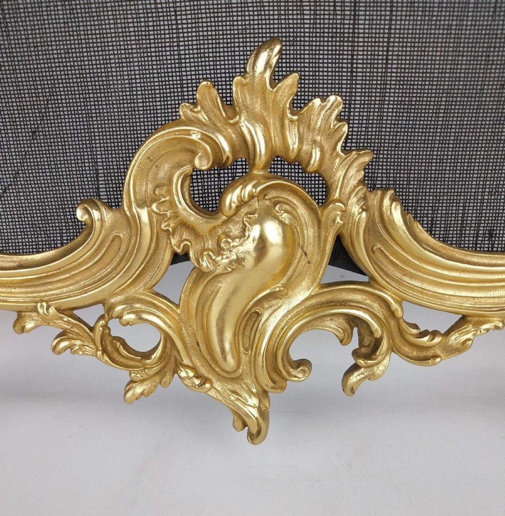 A French Louis XV style gilt bronze fire screen featuring an asymmetrical rocaille frame, central cherub motif, and woven metal mesh. View II