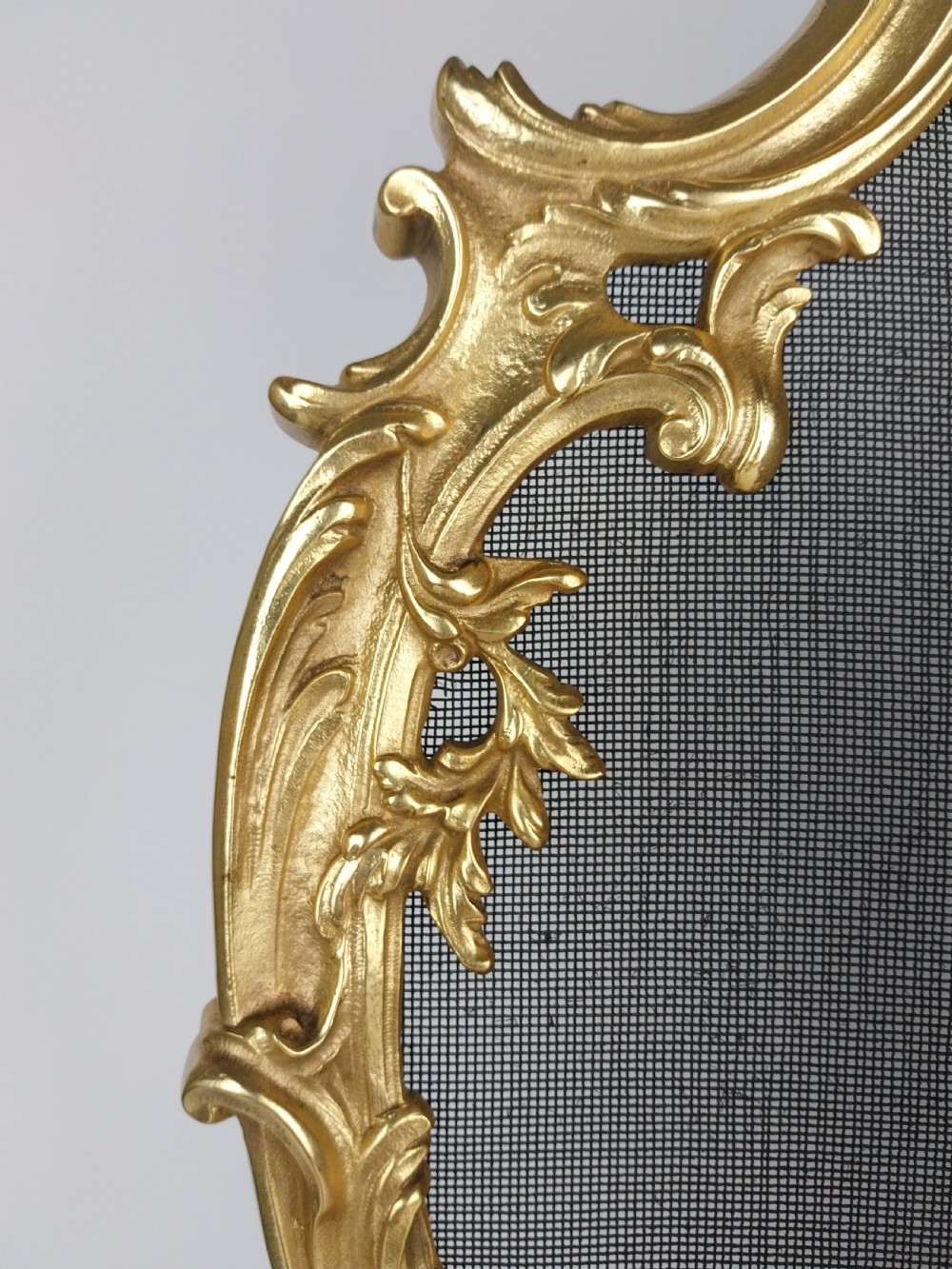 A French Louis XV style gilt bronze fire screen featuring an asymmetrical rocaille frame, central cherub motif, and woven metal mesh. View III