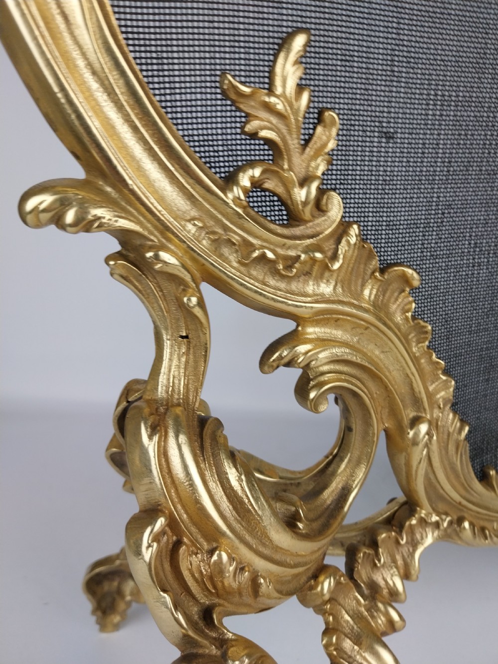 A French Louis XV style gilt bronze fire screen featuring an asymmetrical rocaille frame, central cherub motif, and woven metal mesh. View VI
