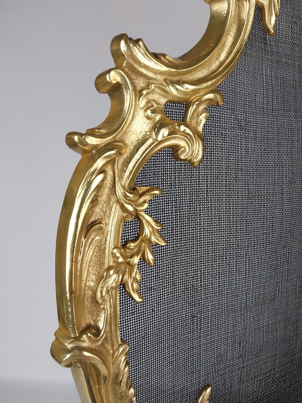 A French Louis XV style gilt bronze fire screen featuring an asymmetrical rocaille frame, central cherub motif, and woven metal mesh. View VII