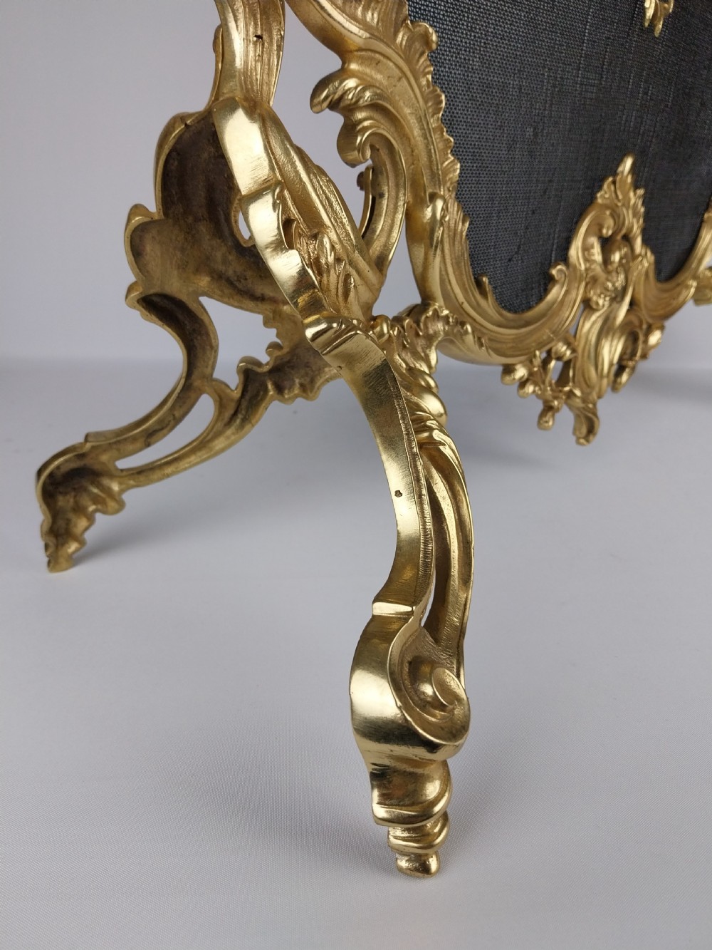 A French Louis XV style gilt bronze fire screen featuring an asymmetrical rocaille frame, central cherub motif, and woven metal mesh. View VIII