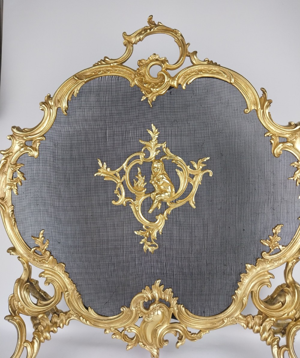 A French Louis XV style gilt bronze fire screen featuring an asymmetrical rocaille frame, central cherub motif, and woven metal mesh. View XI